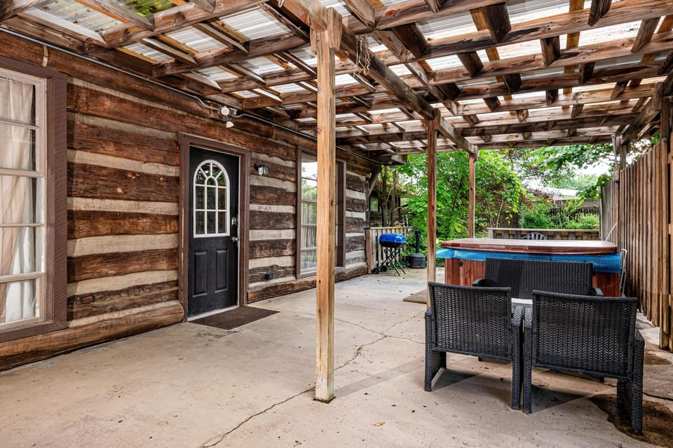 Covered patio with rustic wood beams, concrete floor, black wicker chairs, hot tub, and charcoal grill.