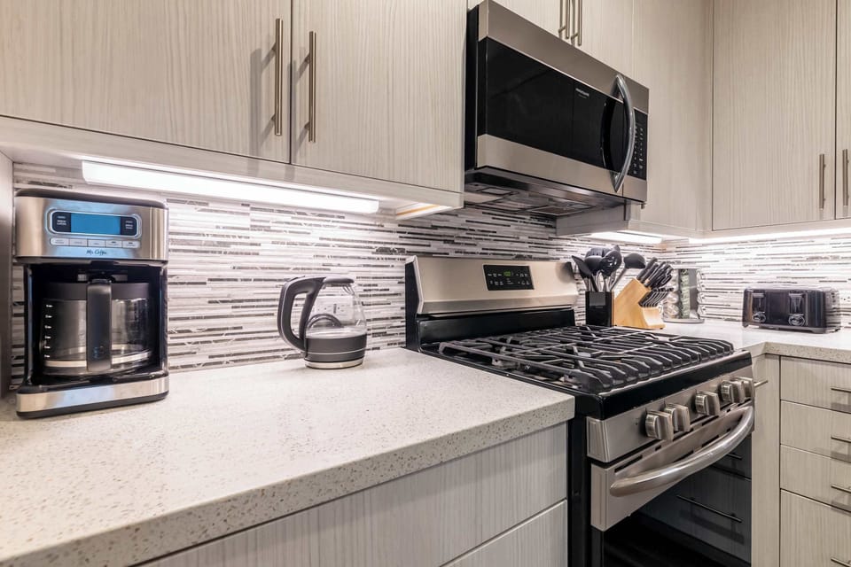 A chef-inspired kitchen featuring soft gray cabinetry, stone countertops, and a full suite of stainless-steel appliances. 