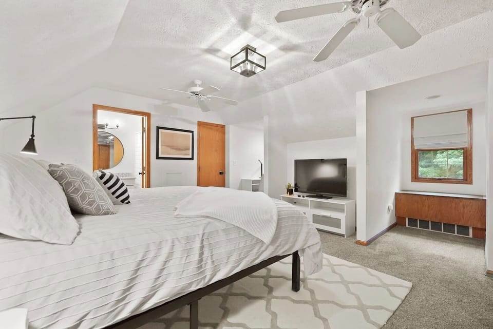 Upstairs primary bedroom with king bed, TV, and ceiling fan