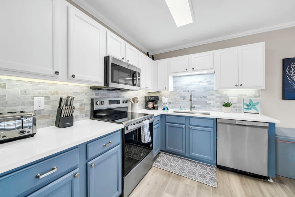 Step into your fully equipped kitchen, where blue and white cabinetry frames stainless steel appliances. A skylight bathes the elegant tile backsplash in natural light, inspiring your culinary adventures.