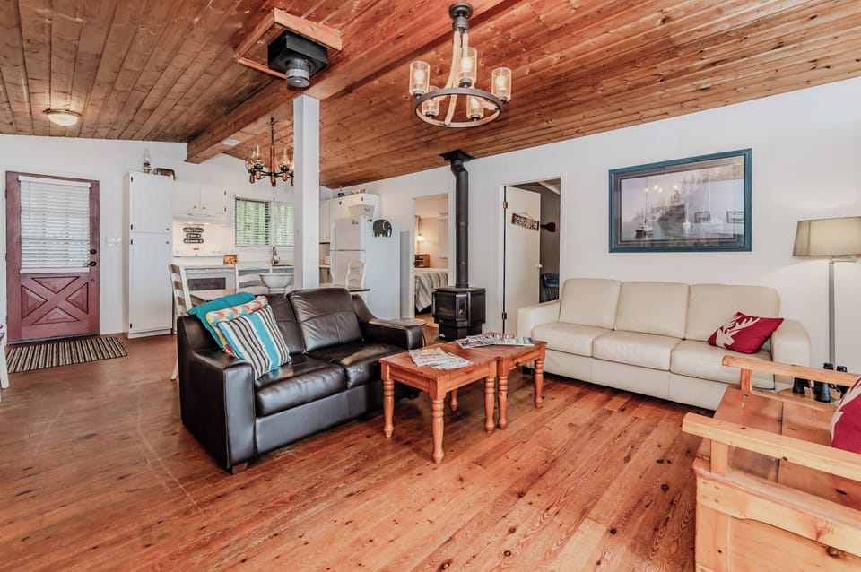 Gather in the inviting living room with comfy seating, rustic wood ceiling, and a wood-burning stove—perfect for cool evenings by the lake.