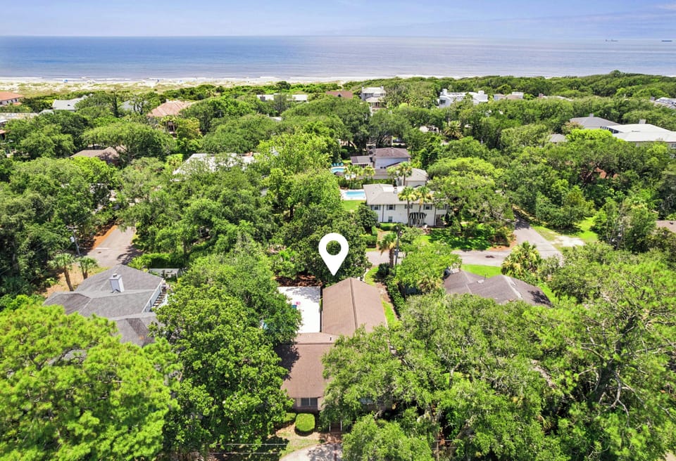 Aerial view showing the property's location within a lush, tree-lined coastal neighborhood, just moments from the beach and ocean beyond.