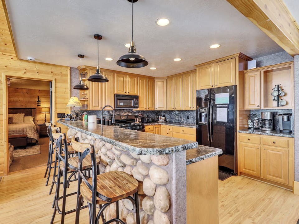 Gourmet kitchen fully equipped with top-of-the-line appliances, stone countertops and backsplash, custom lighting, and a spacious counter with seating for four
