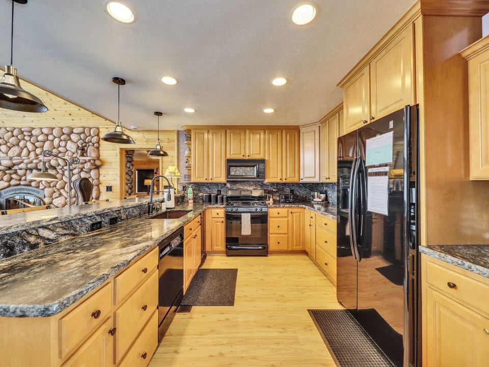 Gourmet kitchen fully equipped with top-of-the-line appliances, stone countertops and backsplash, custom lighting, and a spacious counter with seating for four