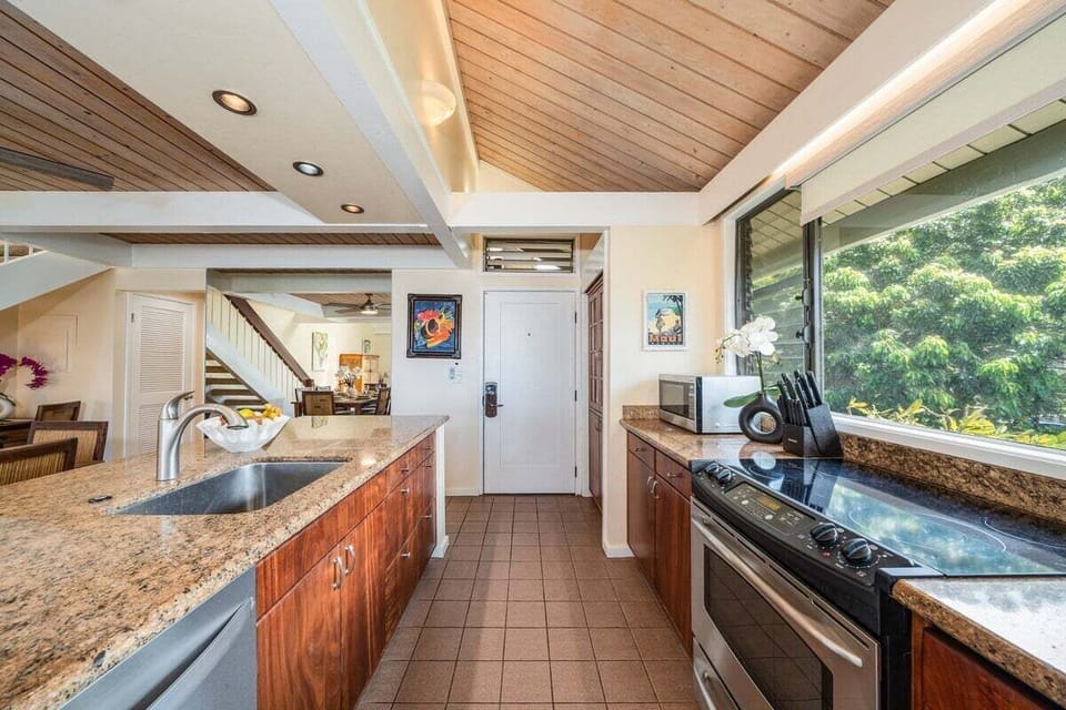 Bright kitchen with granite countertops, stainless steel appliances, and large windows overlooking tropical greenery