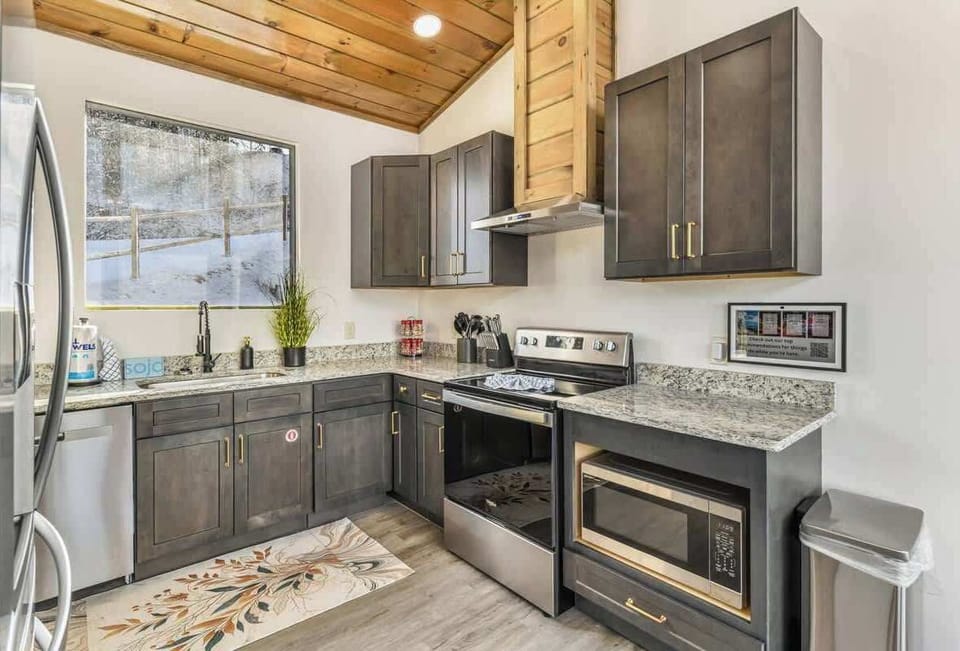 Modern kitchen with dark cabinetry, granite countertops, and stainless steel appliances under a wood-paneled vaulted ceiling.