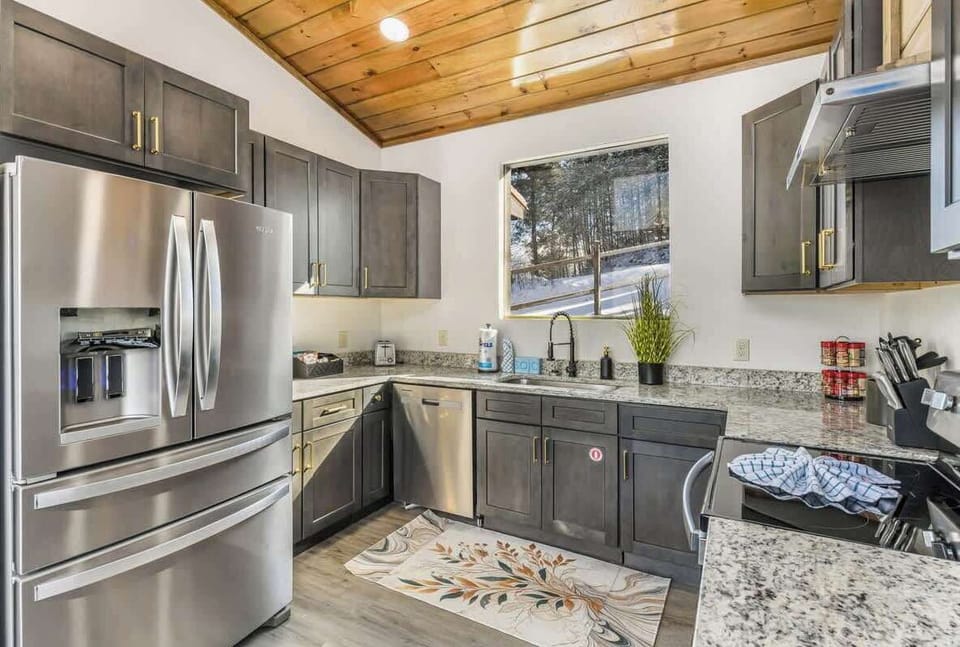 Modern kitchen with stainless steel appliances and granite countertops under a wood-paneled ceiling.