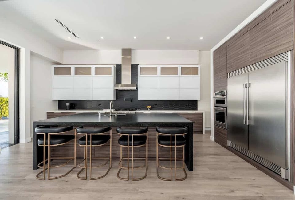 Your sleek, fully-equipped chef's kitchen awaits—picture yourself preparing meals at the spacious island while friends gather on the stylish bar stools, sunlight streaming in through open doors.