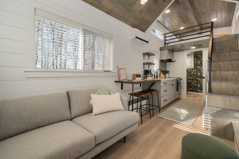Main floor living area at Frost — sofa, kitchenette, and lofted bed above, natural light through the windows