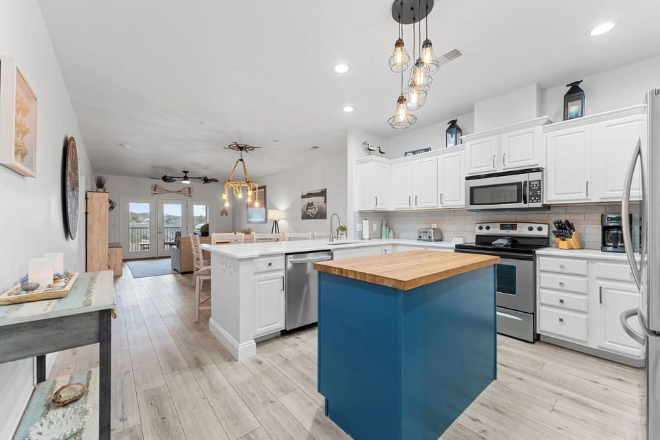 - Bright open layout flows from kitchen to living space with plenty of natural light
- White cabinetry and a bold blue island create a fresh, inviting cook space
- Rustic modern details and warm wooden floor tie the whole gathering area together