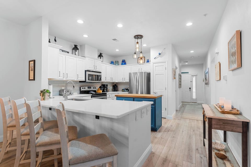 - Fully stocked kitchen with white cabinetry, stainless appliances & cheerful lake accents
- Bold blue island adds a pop of color & extra prep space for group meals
- Light filled open layout flows from kitchen to entry with a relaxed, welcoming vibe