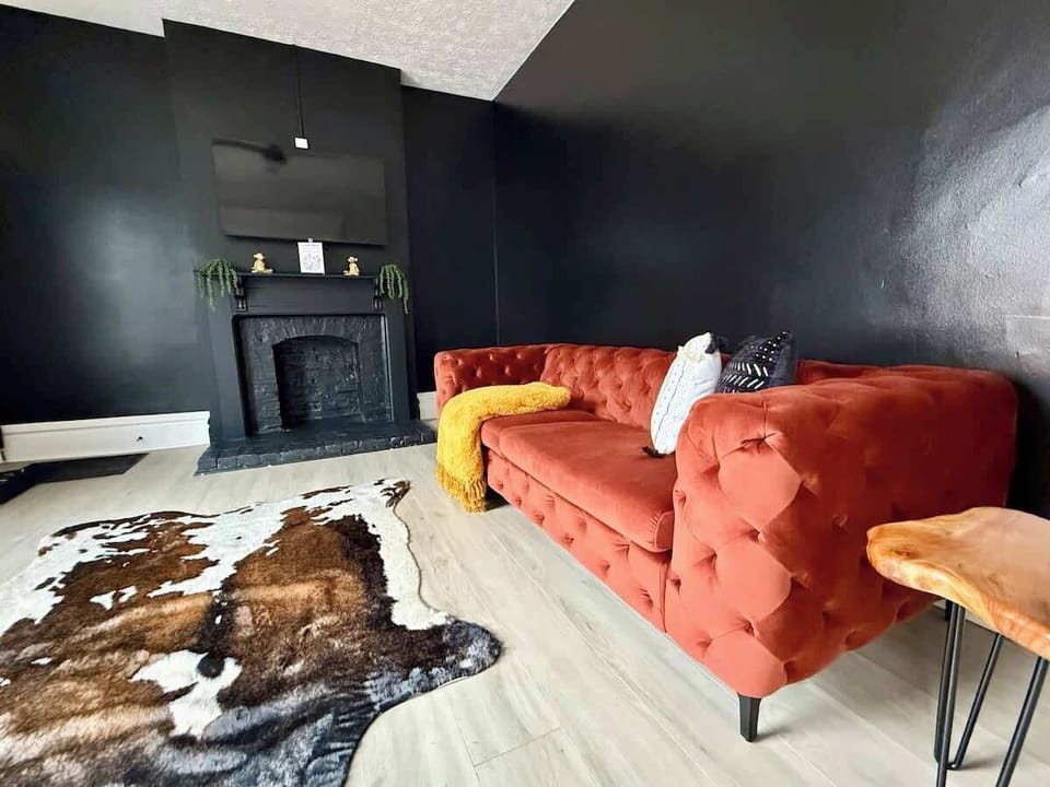 Unwind in style in our modern Jungle House living room in Columbus! Our vibrant orange tufted sofa, cozy yellow throw blanket, and chic cowhide rug create the perfect space to relax. & Our plants are looking forward to hosting you soon 
