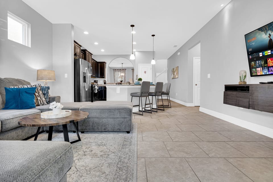 The living room features a cozy sectional sofa, a flatscreen TV, and direct access to the private pool and spa through sliding glass doors.