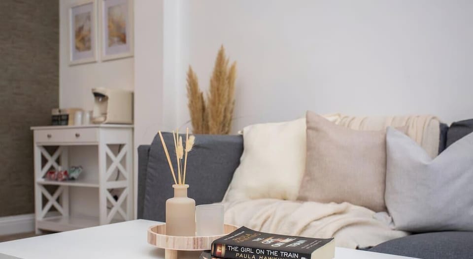 This cozy living space features a comfy sofa with soft, neutral pillows, a minimalist coffee table, and stylish decor—perfect for relaxing with a good book.