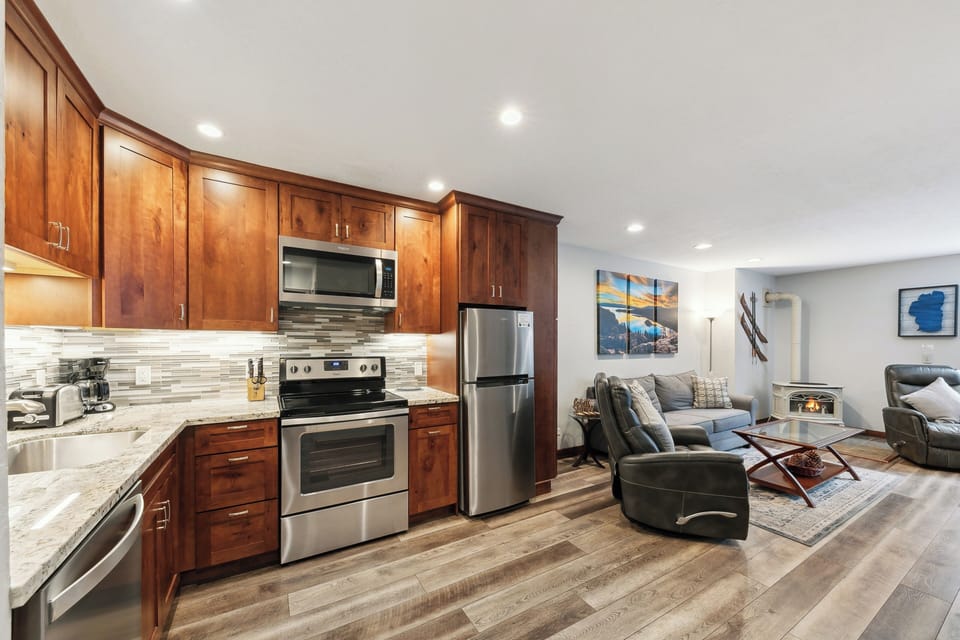 Your fully-equipped kitchen flows seamlessly into a cozy living space with plush leather seating and warm mountain artwork.