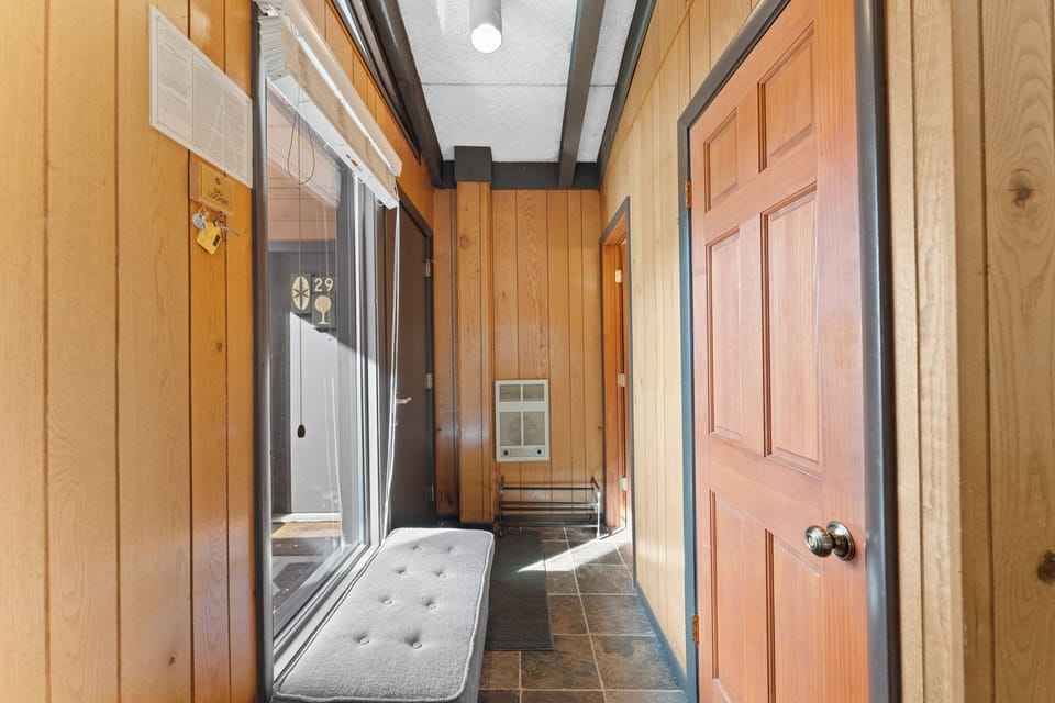 Step through your warm wood-paneled hallway where natural light streams through glass doors, creating a cozy mountain lodge atmosphere.