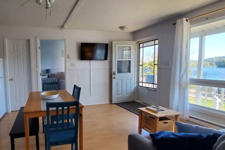 Living room with dining room seating and view of main cottage door to balcony