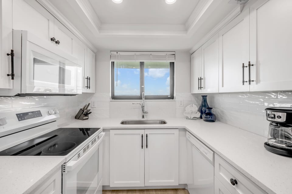 Renovated kitchen with fresh white appliances, cabinets, and countertops—fully equipped for your beach getaway