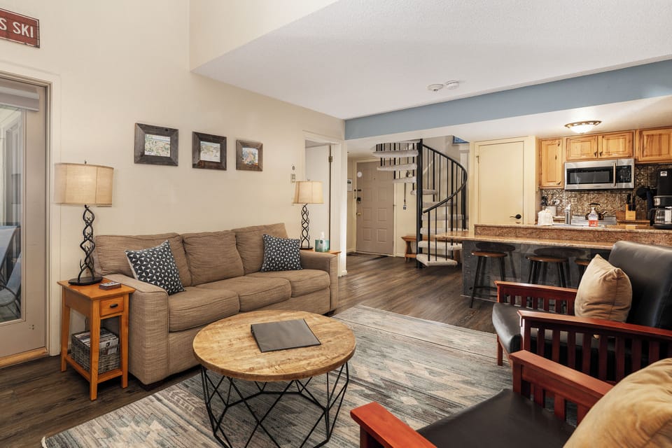 Settle into your cozy open-plan living space at Summit Unit 1303 where warm wood tones and plush seating create the perfect mountain retreat atmosphere.