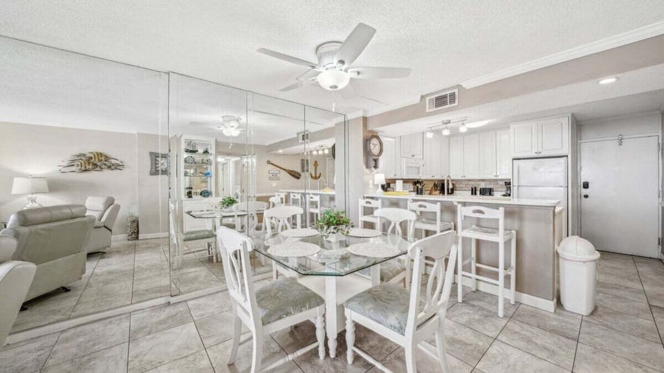 The dining area offers a glass-top table for four and a breakfast bar, creating a bright, inviting space for meals and conversation.