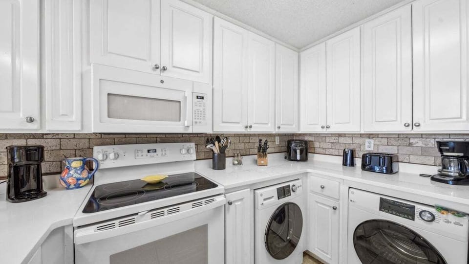 This kitchen has white cabinetry, modern appliances, an in-unit washer/dryer, and all essentials from toaster to air fryer.