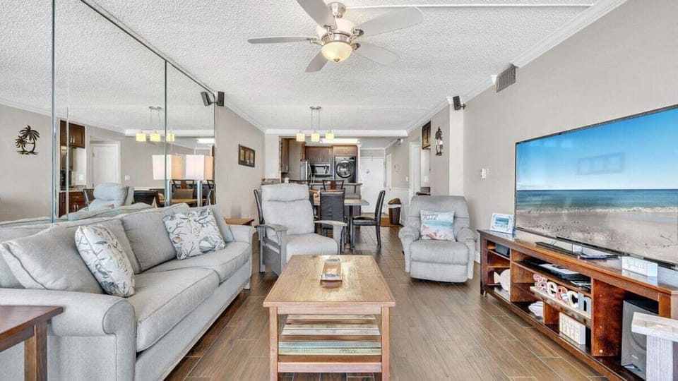 Spacious open-concept living area with cozy recliners, large TV, and Gulf views from the couch. Flows seamlessly into dining and kitchen for easy connection.