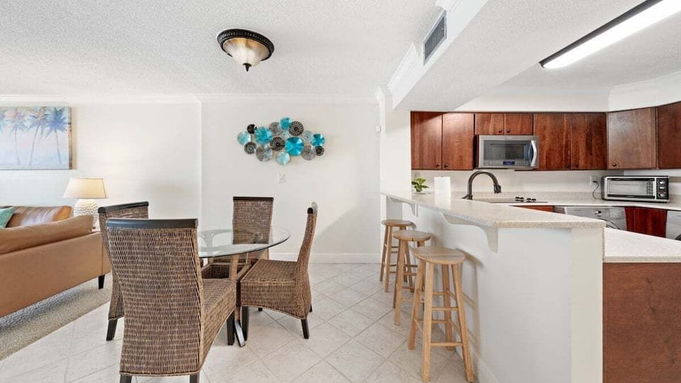 Stylish dining area with wicker seating and glass-top table—perfect for meals or game nights. Kitchen bar with stools adds casual dining and entertaining space.