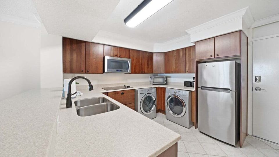 Modern kitchen with sleek stainless steel appliances, in-unit washer and dryer, and ample counter space—perfect for extended stays or beachside meal prep.