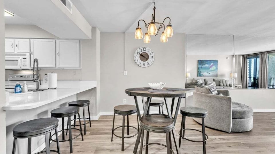 Open dining area with rustic high-top table and bar seating—perfect for casual meals or game nights. Warm lighting and modern coastal vibe complete the space.
