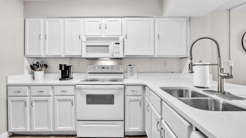 Crisp all-white kitchen with modern appliances, ample cabinetry, and sleek double sink—perfect for cooking vacation meals with ease and style.