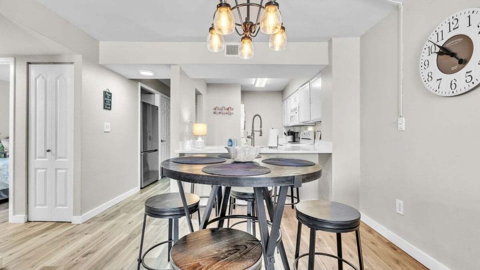 Dining space with rustic high-top table seating five, beneath a warm modern chandelier. Steps from the kitchen, perfect for meals and gatherings.