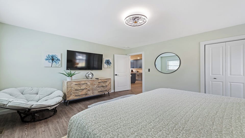 Bedroom features a stylish bed, a comfy lounge chair, and a TV for relaxation.