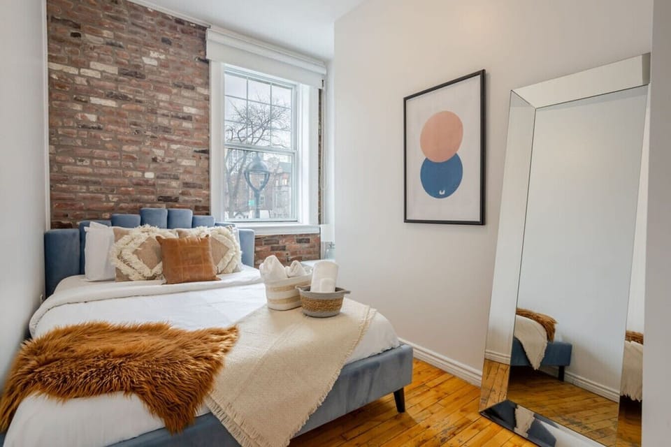 Bedroom #2: Brick feature wall, layered textures, and a full mirror create a bright and stylish retreat