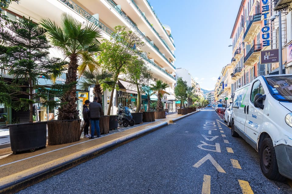Explore the exterior of the apartment, set on a palm-lined street with shops, in the heart of Nice, offering easy access to main attractions.