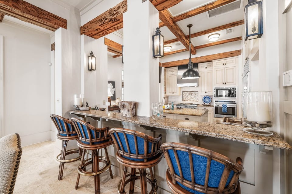 Gather around this stunning granite breakfast bar where rustic wood beams meet coastal elegance—your perfect spot for morning coffee conversations.