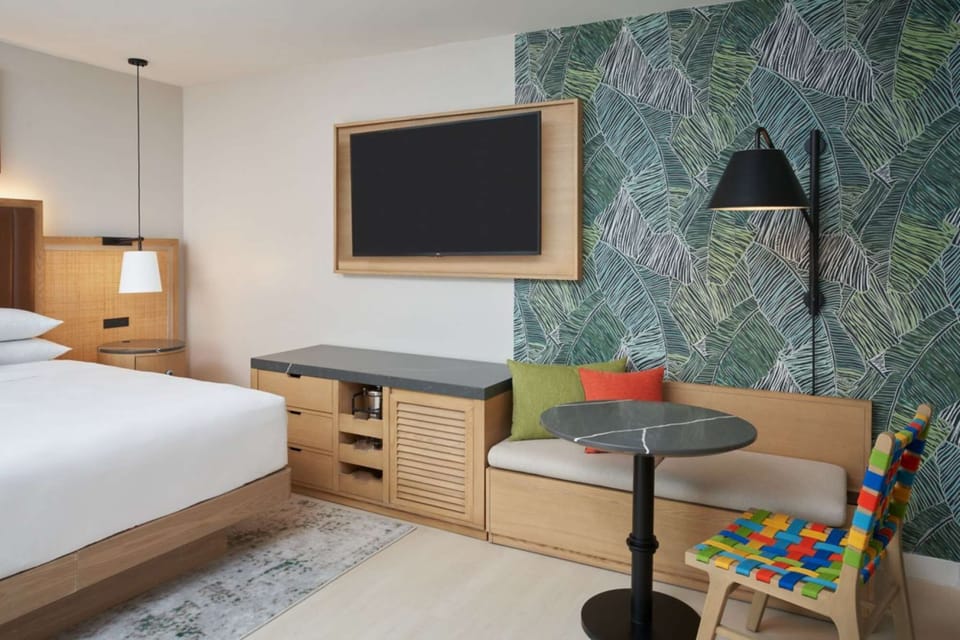 Room with bed, wall TV, bench seat and green leaf wall design