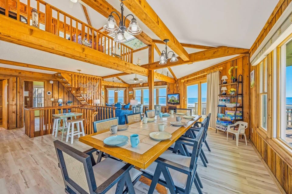 Gather around this spacious dining table where warm wood beams frame ocean views through expansive windows, creating the perfect setting for memorable meals.