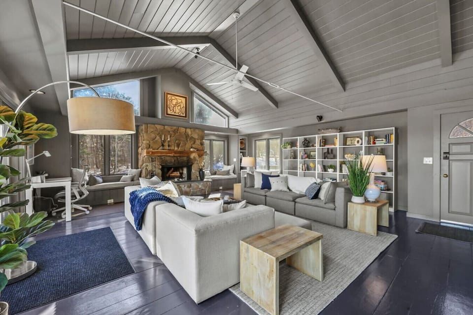Chic, open-concept living room with vaulted, beamed ceilings, a grand stone fireplace, and cozy modern furnishings accented by warm textures.