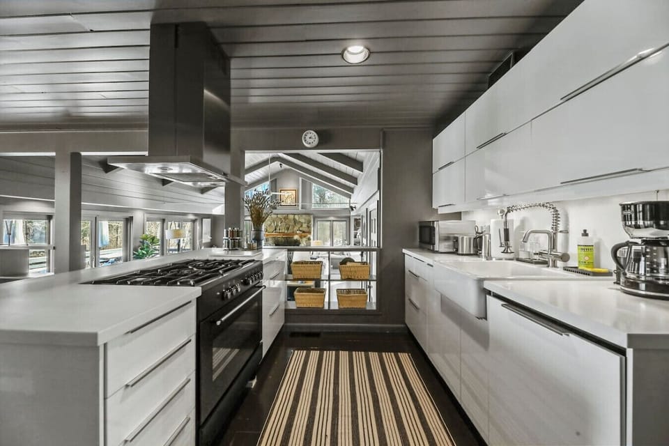 Modern kitchen with sleek white cabinetry, dishwasher,  stainless steel appliances, and a bold striped runner adding warmth and texture.