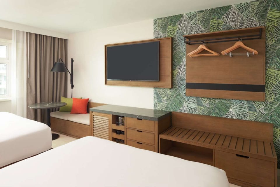 Room with two beds, wall TV, wooden bench and leaf pattern wall