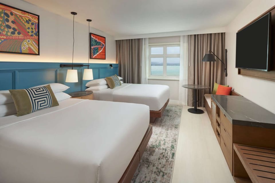 Two beds facing window with sea view and large wall TV