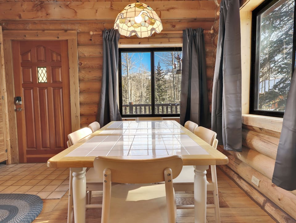 Inviting dining area with a chandelier-lit table for six and large windows showcasing beautiful tree and trails.