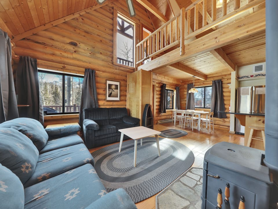 Open-concept view of the living room, loft, and dining area, centered around a cozy wood-burning stove.