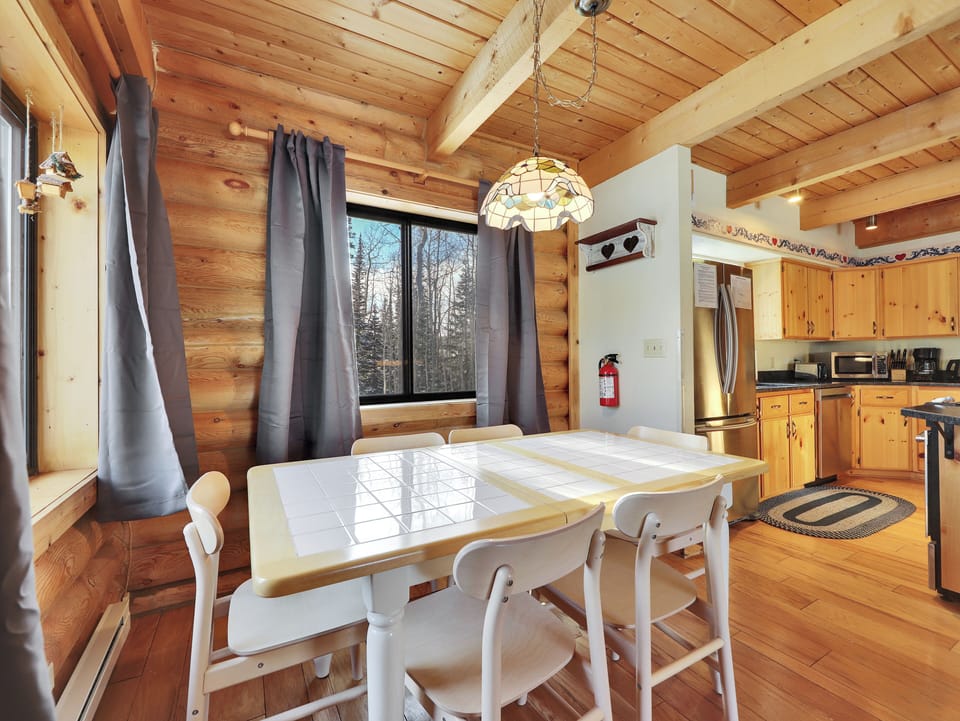 Inviting dining area with a chandelier-lit table for six and large windows showcasing beautiful tree and trails.