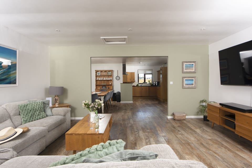 Living area with corner sofa and chairs seating eight, 46 inch Smart TV with Sky package. Patio doors with distant sea views