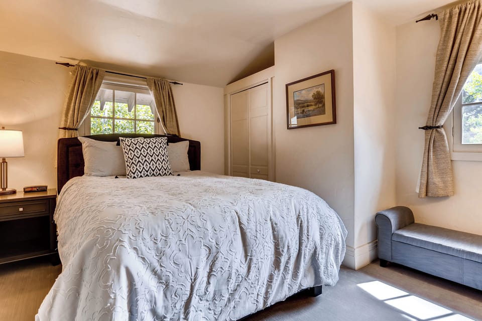 Sunlit bedroom with soft hues, elegant drapes, and cozy seating, creating a serene and welcoming space.