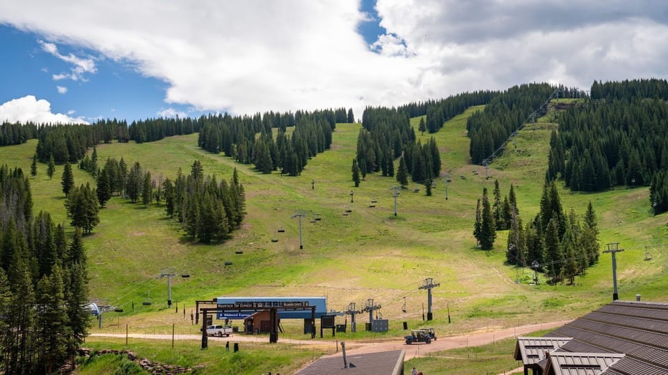 Wide grassy ski runs slope downward past a chairlift terminal under a partly cloudy sky