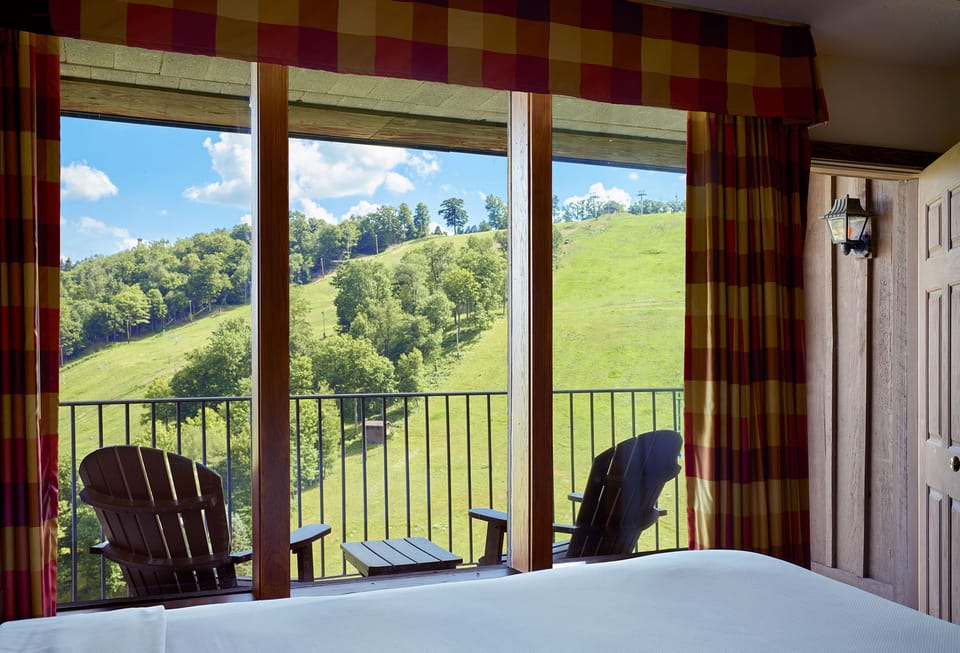 Peaceful bedroom with a balcony view of lush green hills, offering a perfect blend of comfort and natural beauty.