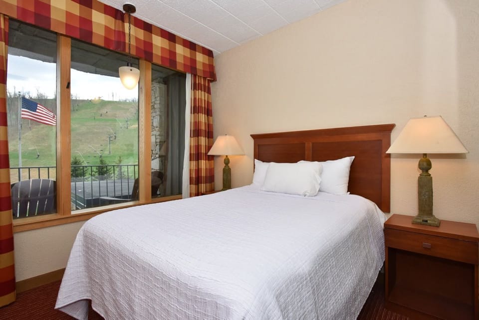 Bright and inviting bedroom featuring a plush bed, soft lighting, and a window framing scenic outdoor views.