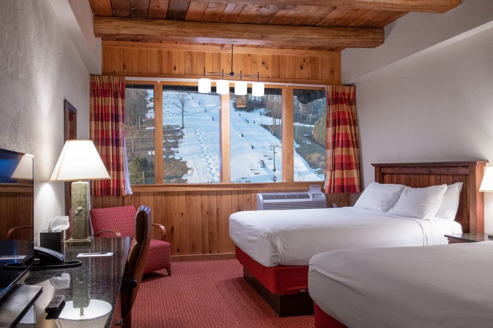 Warm and inviting bedroom with rustic wood accents, cozy twin beds, and a window overlooking a snowy landscape.